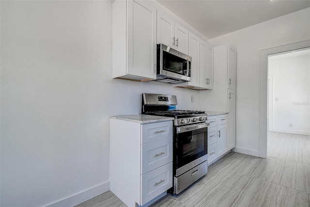 kitchen with baseboards, white cabinets, stainless steel appliances, and light stone counters