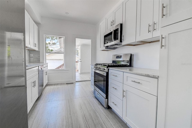 kitchen featuring baseboards, light stone countertops, appliances with stainless steel finishes, white cabinetry, and light wood-type flooring