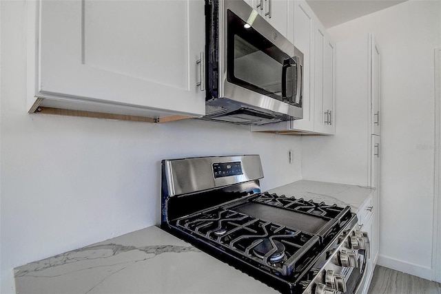 kitchen with appliances with stainless steel finishes, white cabinetry, and light stone countertops