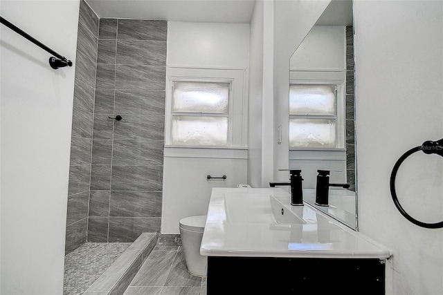 full bathroom with a tile shower, toilet, and vanity