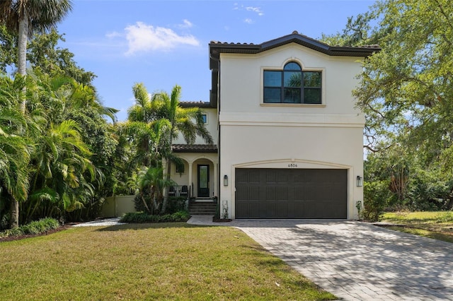 mediterranean / spanish home with a garage, stucco siding, a front yard, decorative driveway, and a tiled roof