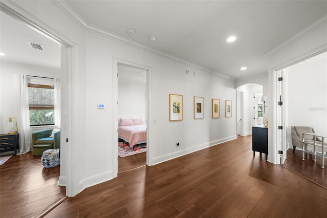 hallway with crown molding, arched walkways, dark wood-style flooring, and visible vents