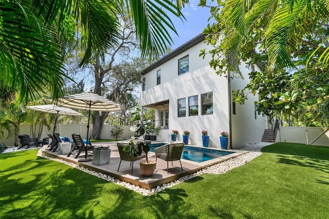 rear view of property with a wooden deck, a fenced backyard, stucco siding, a fenced in pool, and a lawn