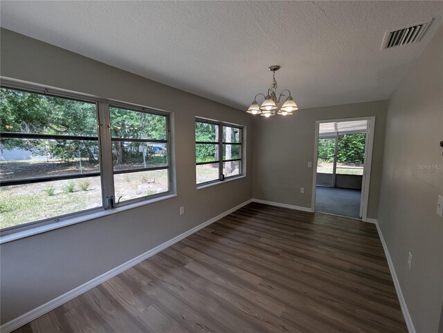 empty room featuring a notable chandelier, a textured ceiling, baseboards, dark wood-type flooring, and visible vents