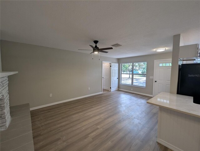 unfurnished living room featuring a ceiling fan, visible vents, a fireplace, baseboards, and dark wood-type flooring