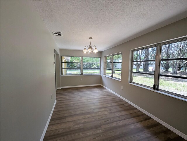 unfurnished dining area featuring a notable chandelier, a textured ceiling, dark wood finished floors, baseboards, and visible vents