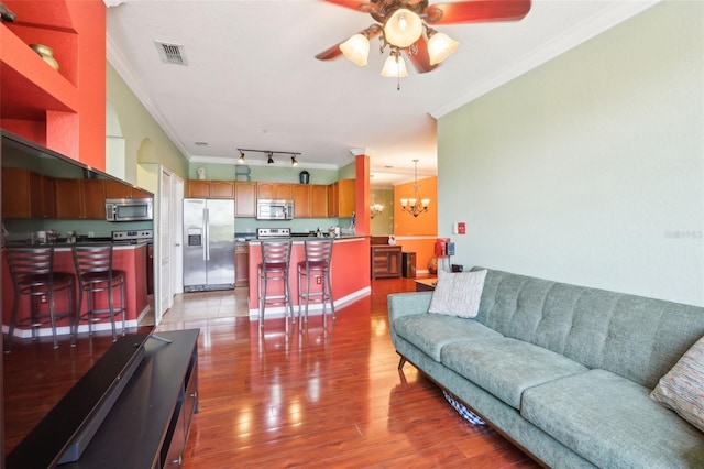living area featuring visible vents, ornamental molding, ceiling fan with notable chandelier, and wood finished floors