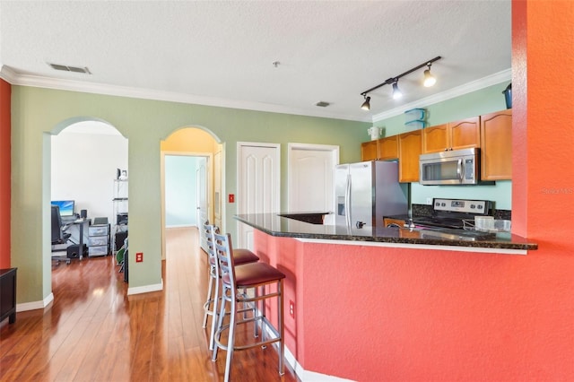 kitchen with crown molding, a textured ceiling, hardwood / wood-style floors, stainless steel appliances, and visible vents