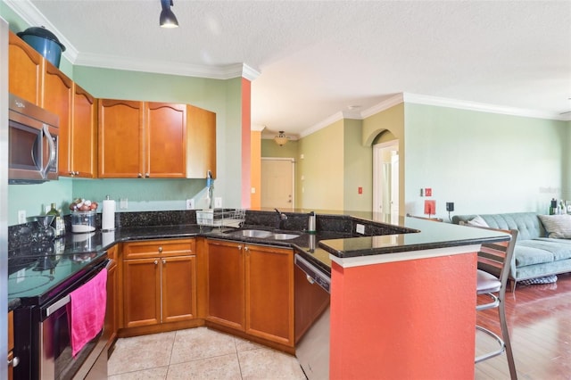 kitchen featuring crown molding, brown cabinetry, open floor plan, a sink, and stainless steel appliances