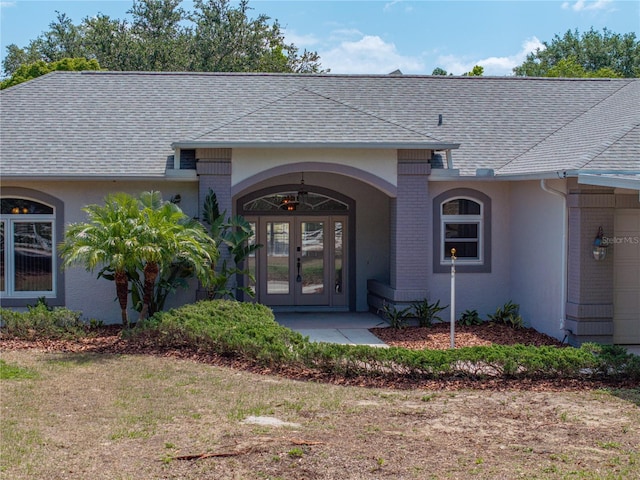 view of exterior entry with roof with shingles, an attached garage, french doors, and brick siding