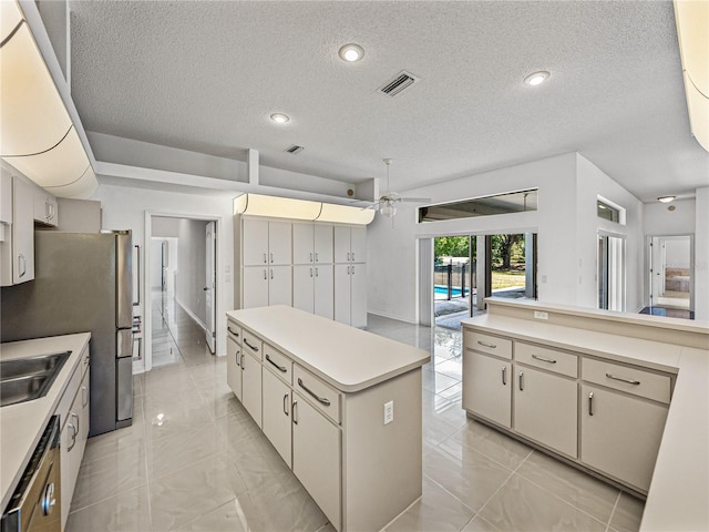 kitchen featuring light countertops, a kitchen island, marble finish floor, ceiling fan, and a textured ceiling