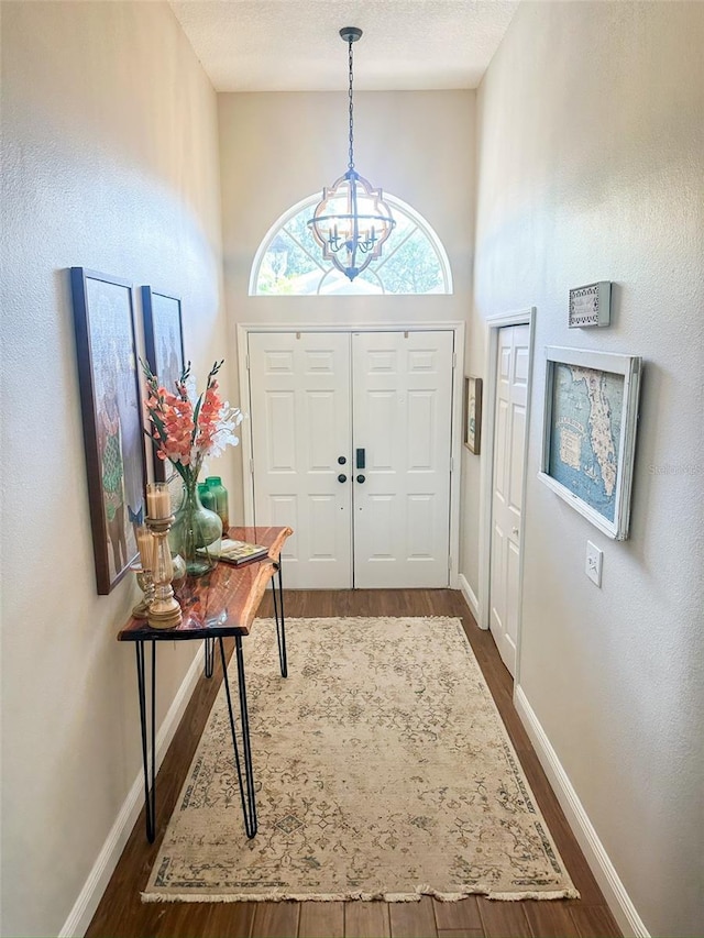 foyer entrance featuring a chandelier, baseboards, and dark wood-type flooring