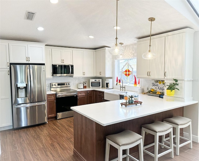 kitchen with appliances with stainless steel finishes, white cabinets, a sink, visible vents, and a peninsula