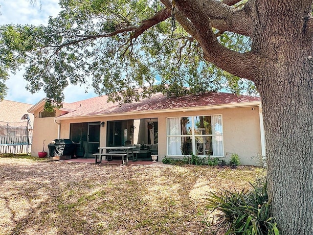 rear view of house featuring a patio area, stucco siding, a sunroom, and fence