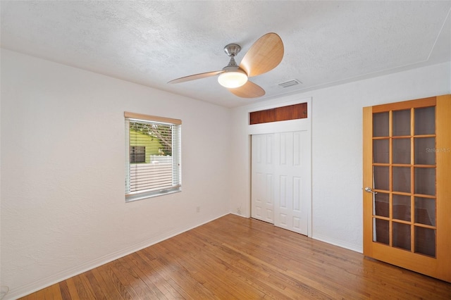 unfurnished bedroom featuring visible vents, a closet, baseboards, a textured ceiling, and hardwood / wood-style flooring