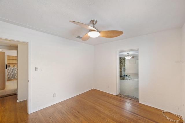 empty room featuring baseboards, a ceiling fan, wood finished floors, and visible vents