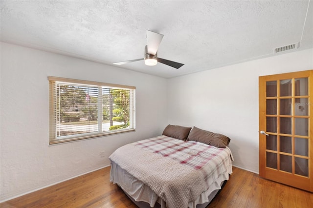 bedroom featuring visible vents, wood finished floors, baseboards, ceiling fan, and a textured ceiling