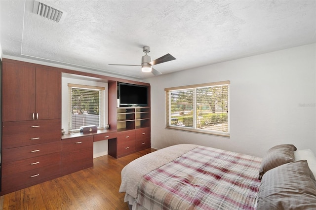 bedroom featuring a textured ceiling, multiple windows, wood finished floors, and visible vents