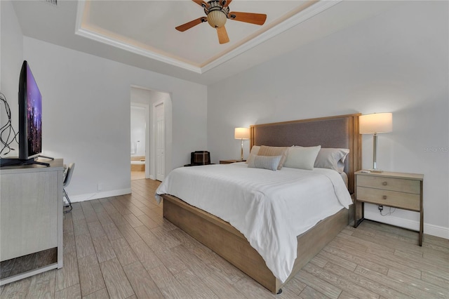 bedroom featuring ceiling fan, ensuite bath, baseboards, wood finished floors, and a tray ceiling