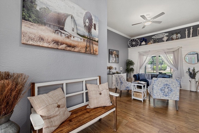 living area with a textured wall, ceiling fan, ornamental molding, and wood finished floors