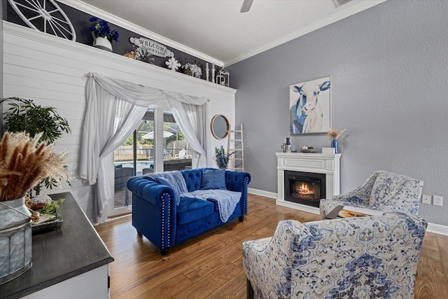 living room featuring ornamental molding, a glass covered fireplace, wood finished floors, baseboards, and ceiling fan