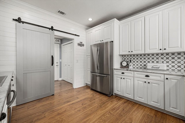 kitchen with white cabinets, a barn door, freestanding refrigerator, wood finished floors, and visible vents