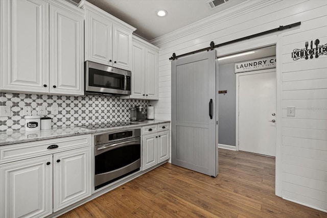 kitchen with appliances with stainless steel finishes, white cabinets, backsplash, and a barn door