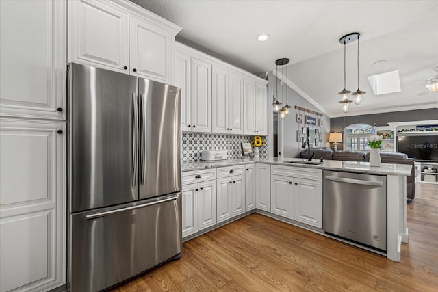 kitchen featuring ornamental molding, open floor plan, vaulted ceiling with skylight, a sink, and appliances with stainless steel finishes