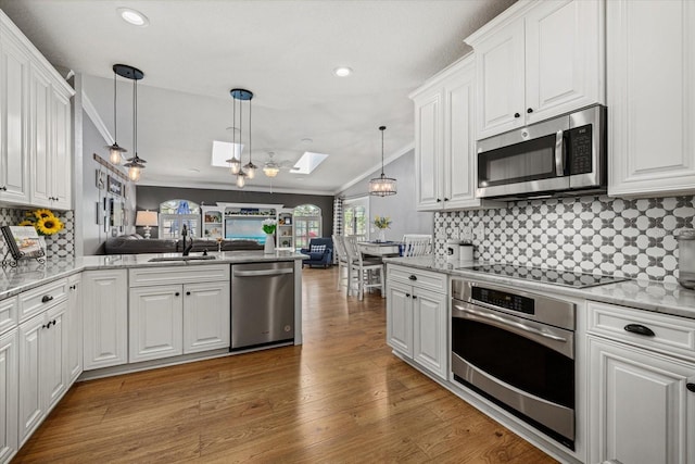 kitchen with crown molding, appliances with stainless steel finishes, open floor plan, light wood-style floors, and white cabinetry