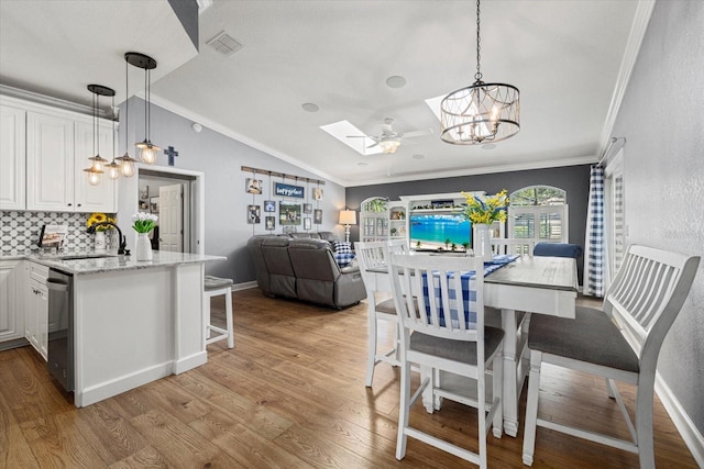 dining space with visible vents, ornamental molding, lofted ceiling with skylight, light wood-type flooring, and a chandelier