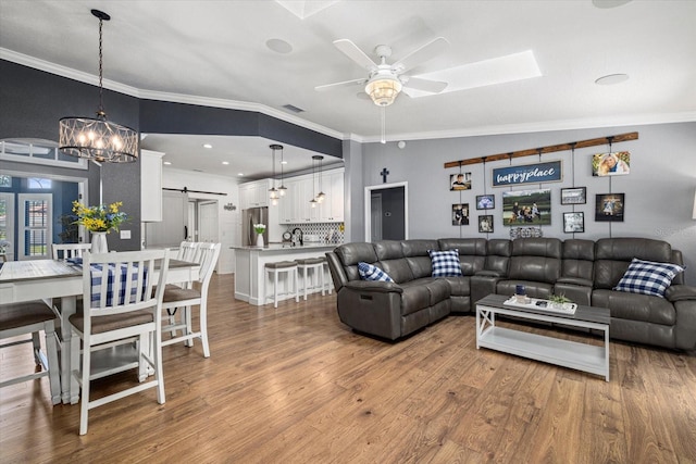 living area with crown molding, ceiling fan with notable chandelier, a barn door, and wood finished floors