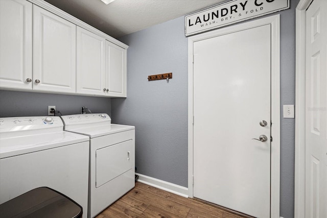 clothes washing area featuring cabinet space, baseboards, wood finished floors, and washer and dryer