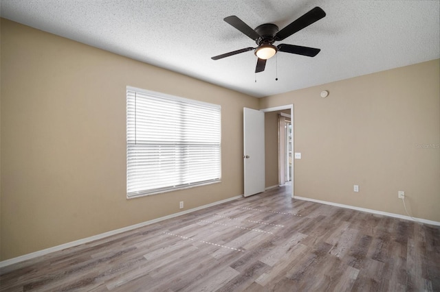 empty room featuring baseboards, wood finished floors, a ceiling fan, and a textured ceiling