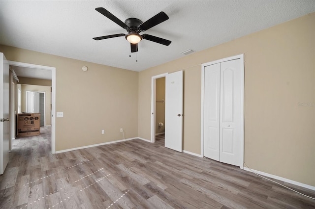 unfurnished bedroom featuring wood finished floors, a closet, baseboards, visible vents, and a textured ceiling