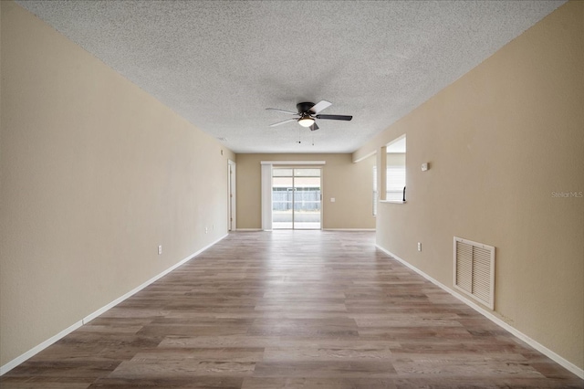 unfurnished room featuring wood finished floors, ceiling fan, baseboards, visible vents, and a textured ceiling