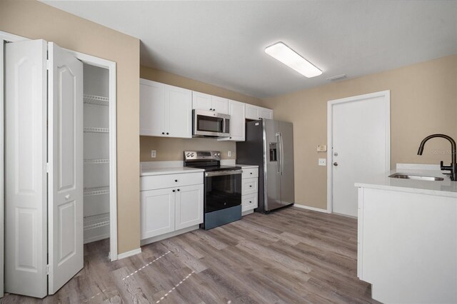 kitchen featuring white cabinetry, appliances with stainless steel finishes, light wood finished floors, and a sink