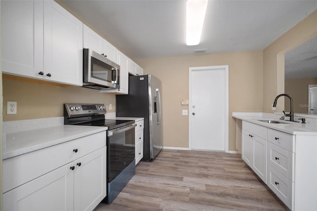 kitchen with white cabinetry, a sink, appliances with stainless steel finishes, light countertops, and light wood finished floors