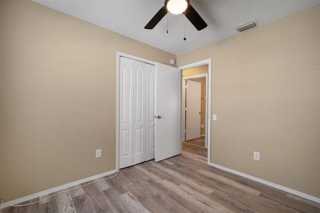 unfurnished bedroom with visible vents, ceiling fan, a closet, baseboards, and wood finished floors