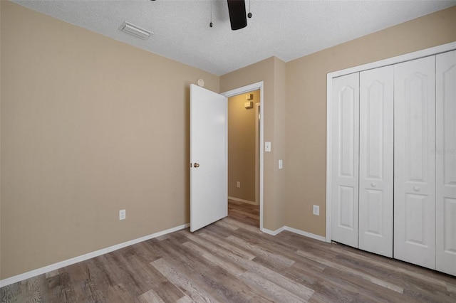 unfurnished bedroom with a closet, visible vents, baseboards, a textured ceiling, and wood finished floors