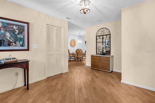 hallway featuring baseboards, light wood-style flooring, a chandelier, and visible vents