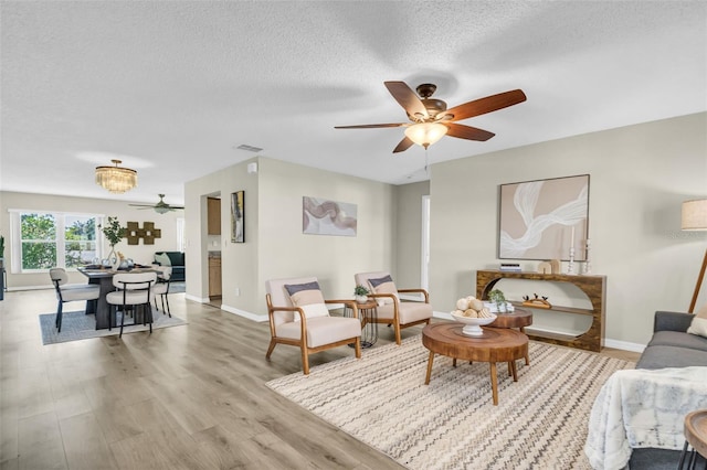 living area with ceiling fan, light wood-type flooring, a textured ceiling, and baseboards