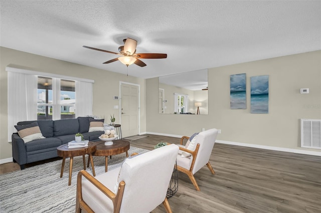 living room featuring healthy amount of natural light, wood finished floors, a ceiling fan, baseboards, and a textured ceiling