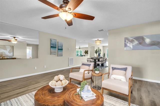 living room featuring a ceiling fan, wood finished floors, baseboards, and a textured ceiling