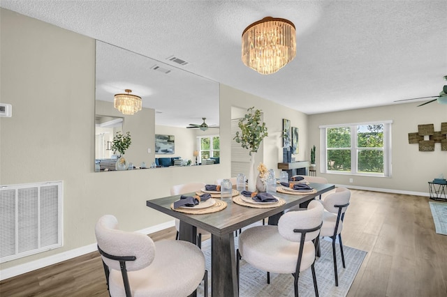 dining space featuring ceiling fan, a textured ceiling, wood finished floors, baseboards, and a chandelier