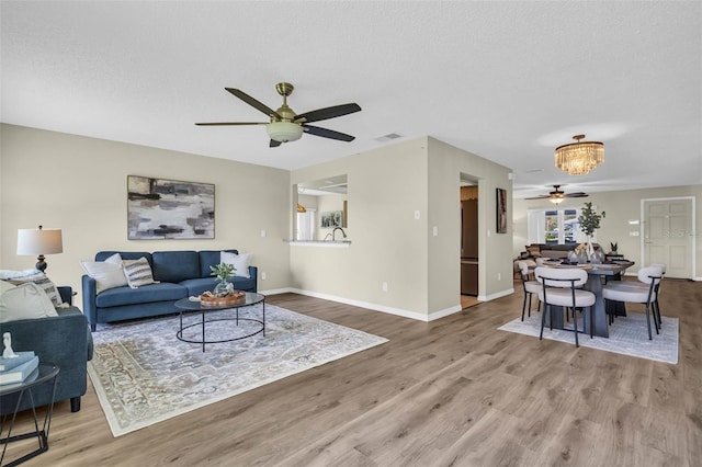 living area featuring ceiling fan, wood finished floors, baseboards, and a chandelier