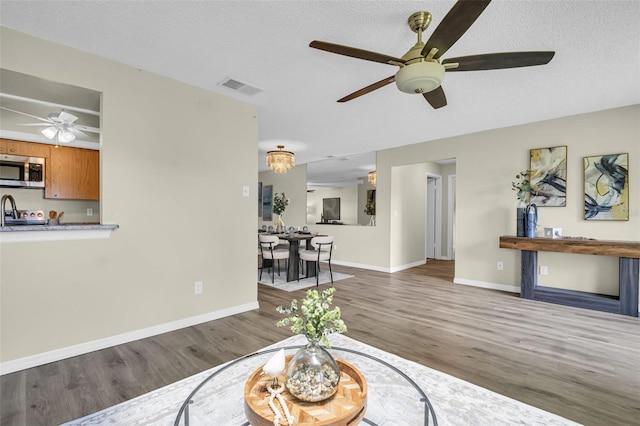 living area with a ceiling fan, wood finished floors, baseboards, and a textured ceiling