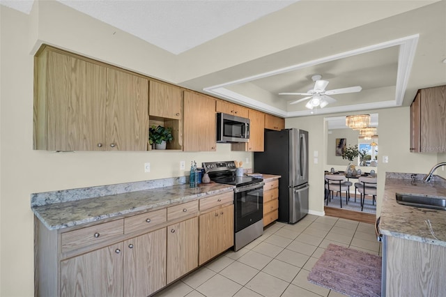 kitchen with appliances with stainless steel finishes, a sink, a tray ceiling, light tile patterned floors, and a ceiling fan