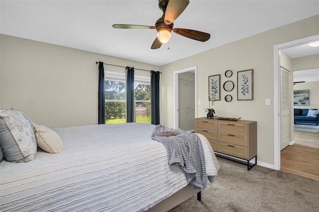 bedroom with light colored carpet, baseboards, ceiling fan, a walk in closet, and a closet