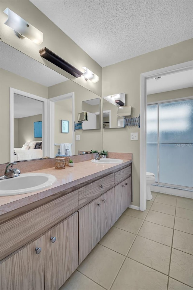 ensuite bathroom featuring double vanity, tile patterned floors, toilet, a textured ceiling, and an enclosed shower
