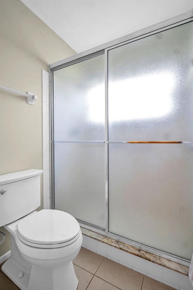 bathroom featuring tile patterned flooring, toilet, and a stall shower